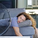 Young woman lying in front of the electric fan at home, overwhelmed by the heat