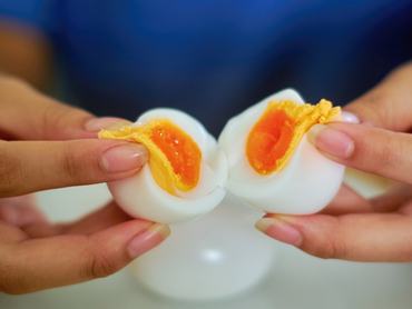 A close-up view of two hands gently splitting a soft-boiled egg, revealing its golden, runny yolk. The image showcases the delicate texture of the egg, with the creamy yolk oozing out against the smooth, cooked egg white.