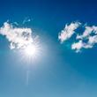 Bright sun shining through fluffy white clouds in deep blue sky