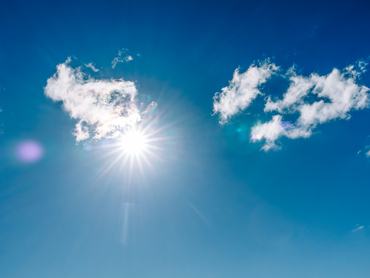 Bright sun shining through fluffy white clouds in deep blue sky